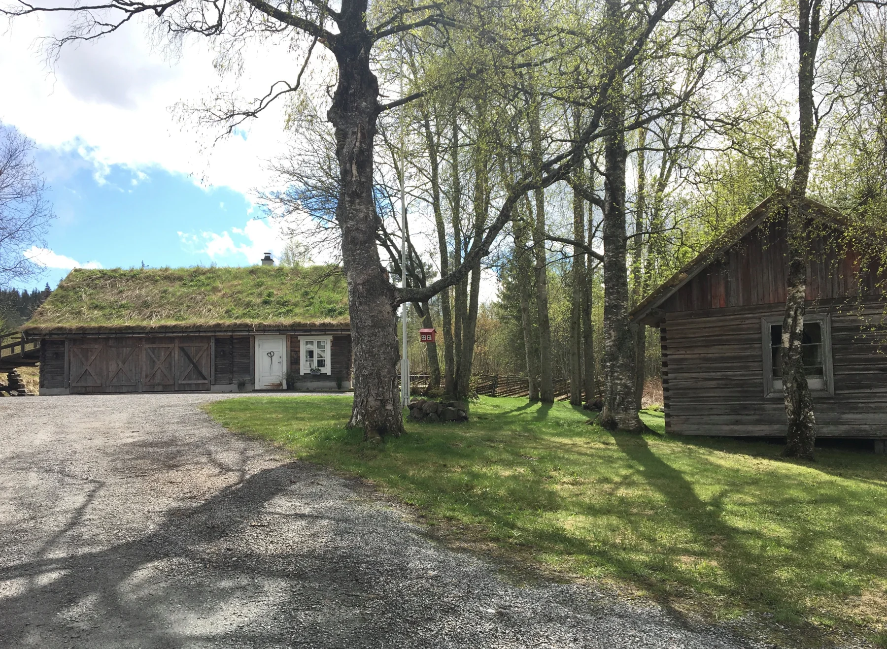 Gårdstunet på Nærby gård med trær og tradisjonelle trehus.